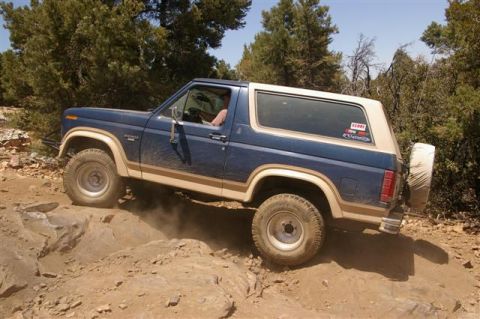 1986 Ford Bronco - A blue and tan Ford Bronco navigates a challenging, rocky off-road path.