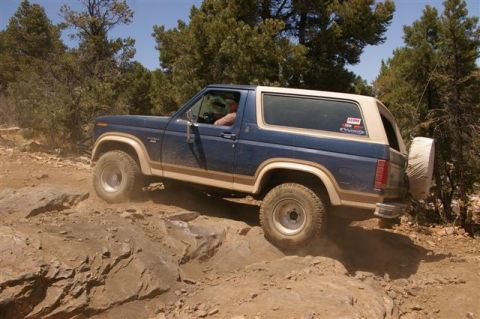 1986 Ford Bronco - This 1986 Ford Bronco is shown tackling a challenging off-road trail with steep rocks and dusty conditions.