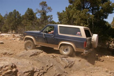 1986 Ford Bronco - This Ford Bronco is navigating a rocky off-road trail with trees in the background.