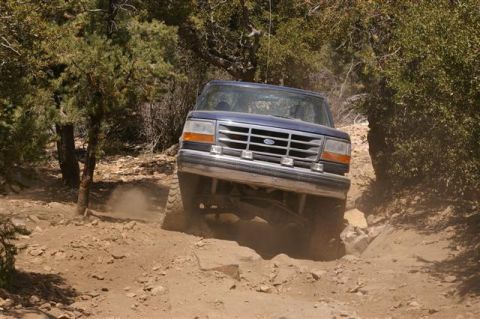 1986 Ford Bronco - This blue Ford Bronco navigates a challenging off-road trail, kicking up dust as it goes.