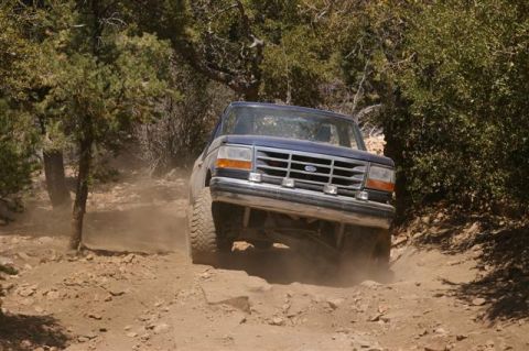 1986 Ford Bronco - A blue Ford Bronco navigates a dusty, rocky trail.