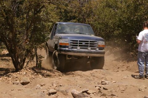 1986 Ford Bronco - Ford Bronco navigates a challenging off-road path, kicking up dust.
