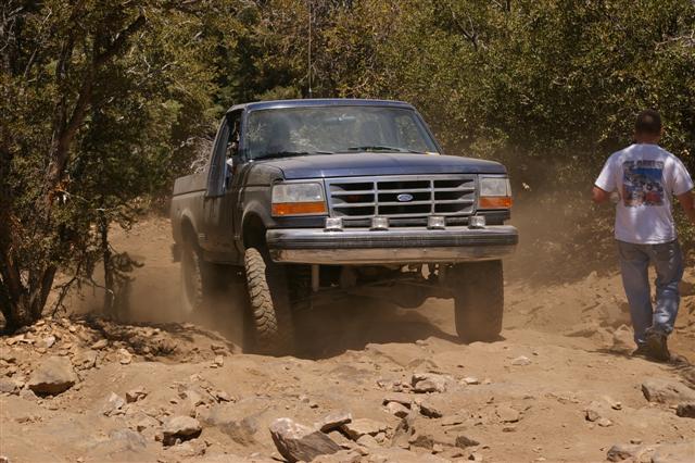 Blue Ford F-Series truck driving on a dirt trail with a man walking nearby