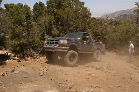 1986 Ford Bronco - A black Ford Bronco navigates a dusty, rocky off-road trail.