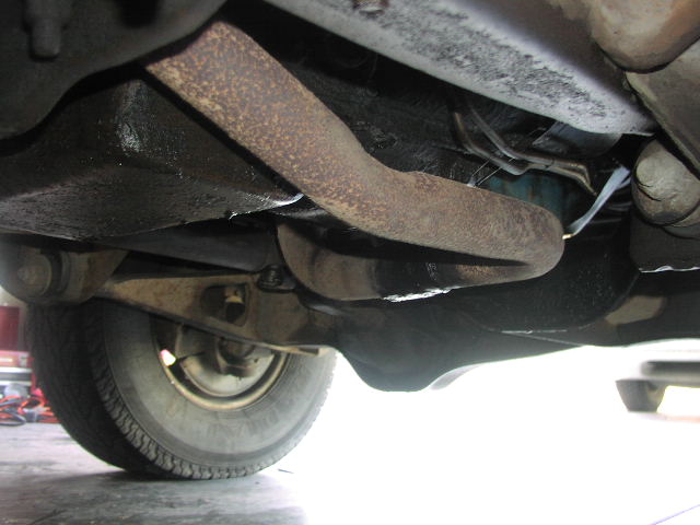 Underside view of vehicle suspension, showing a tire and rusty metal components