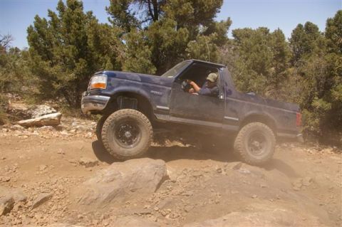 1986 Ford Bronco - This blue Ford Bronco is navigating a rocky off-road trail with a driver behind the wheel.