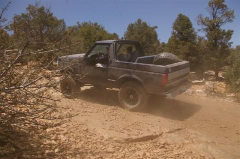 1986 Ford Bronco - A Ford Bronco navigates a challenging off-road path, kicking up dust.