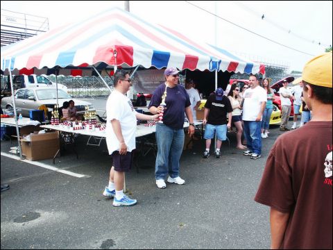 2001 Mercury Grand Marquis - A silver sedan is visible behind a table of trophies at an outdoor car show.