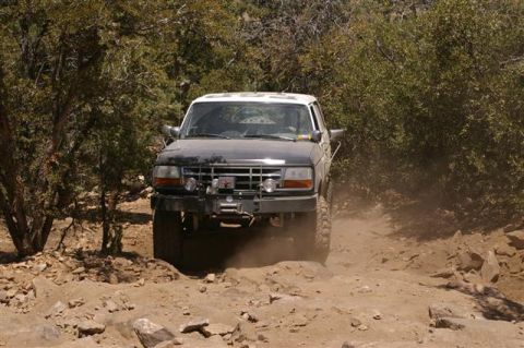 1986 Ford Bronco - A Ford Bronco navigates a rocky, off-road trail surrounded by trees.
