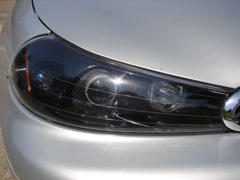 1992 Ford Taurus - The driver's side headlight assembly of a silver car is shown in detail, a black housing and clear lens.