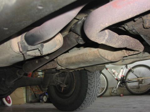 1981 Ford Bronco - The underside of a vehicle reveals its exhaust system and rear axle components, with a bicycle visible behind.