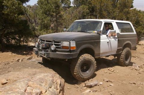 1986 Ford Bronco - This modified Ford Bronco navigates a challenging off-road trail with large tires and a winch.