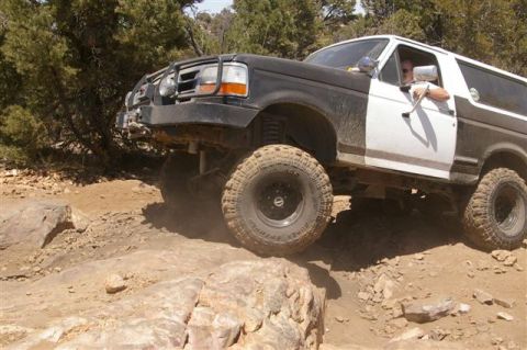 1986 Ford Bronco - This modified Ford Bronco is tackling a challenging off-road course with large rocks and loose dirt.