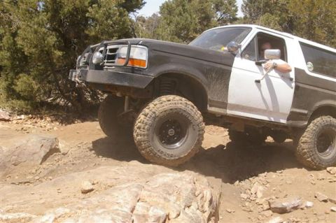 1986 Ford Bronco - This lifted Ford Bronco, likely from the early 1990s, tackles a challenging off-road course with large tires and a modified bumper.