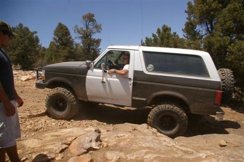 1986 Ford Bronco - Ford Bronco tackles a challenging off-road trail under a clear blue sky.