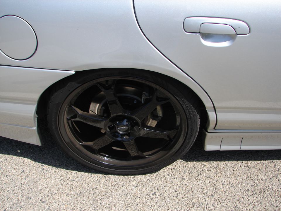 Silver sedan rear wheel with black aftermarket rims and lowered suspension