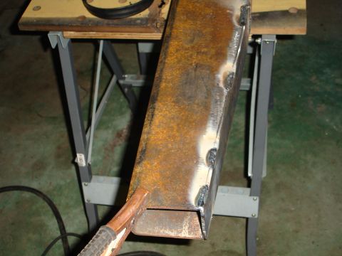 1989 Ford Bronco - A metal beam is being welded on a workbench, with a welding clamp attached to it.