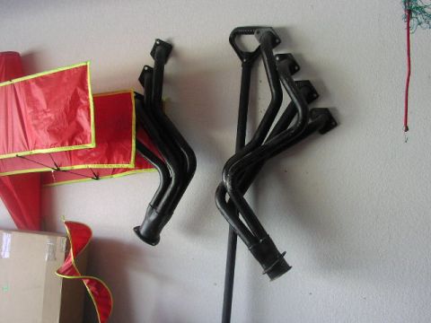 1981 Ford Bronco - Pair of exhaust headers on a wall next to red fabric panels.