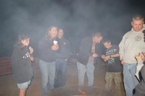 1986 Ford Bronco - A group of people are gathered around a fire pit, with smoke obscuring the background.