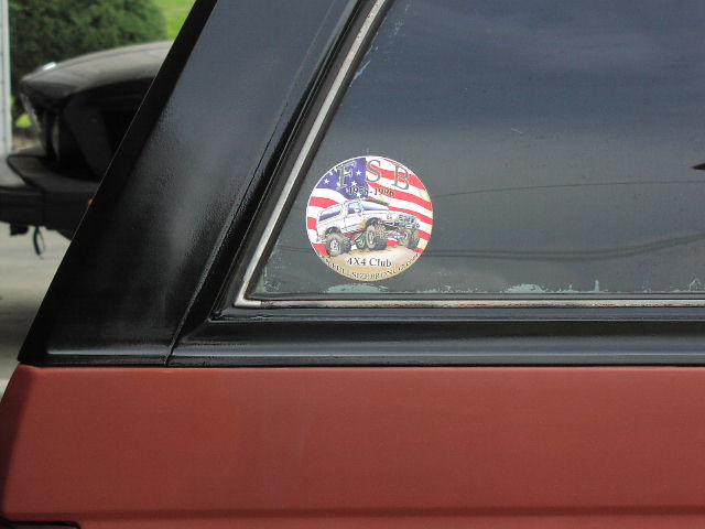 sticker on window shows two lifted trucks, one with American flag background