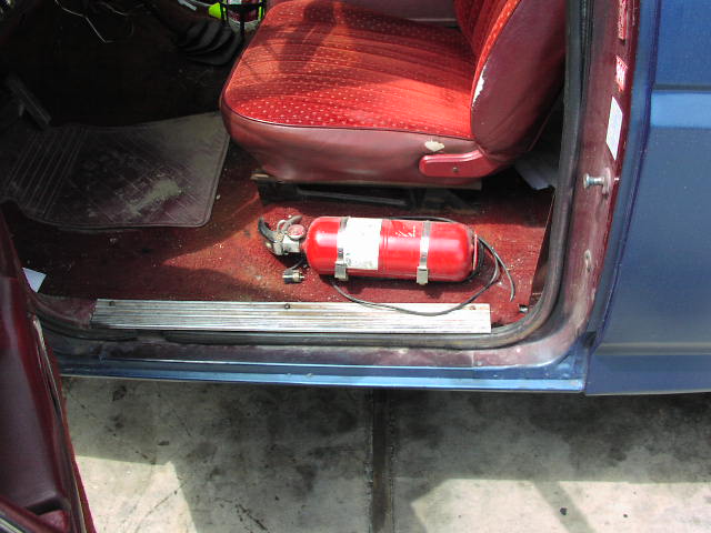 Interior of a blue vehicle showing a red fire extinguisher on the floor next to a red patterned seat