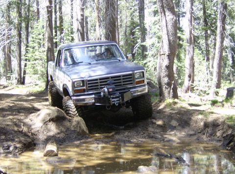 1986 Ford Bronco - This truck navigates a muddy obstacle course in a forest setting.