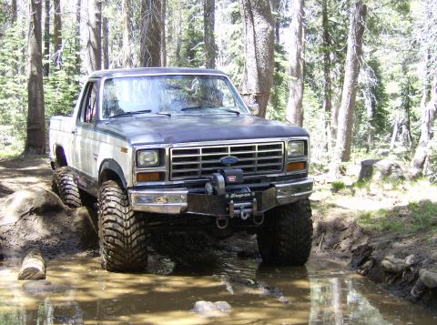1986 Ford Bronco - Modified 1980s Ford pickup truck navigates a muddy trail in a forest setting.