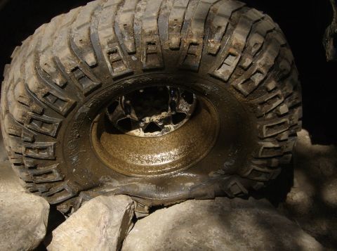 1986 Ford Bronco - A close-up view of a muddy off-road tire with a flat spot, positioned on large rocks.