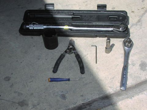 1981 Ford Bronco - A collection of tools, including a torque wrench, socket, pliers, screwdriver, and Allen wrench, laid out on a concrete surface.