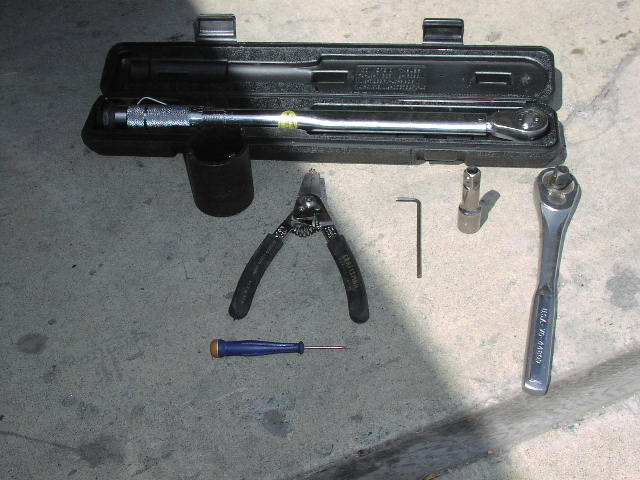 Tools on concrete: torque wrench in case, socket, snap-ring pliers, wrench, screwdriver.