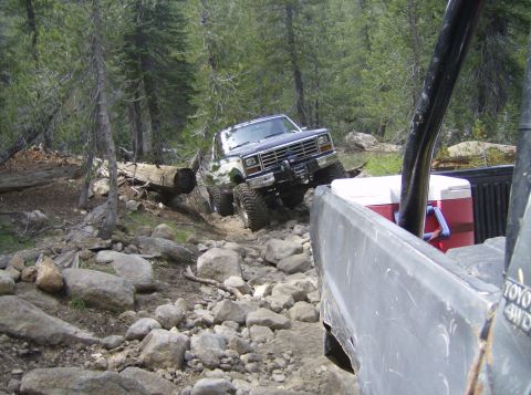 1986 Ford Bronco - A dark blue 1980s Ford Bronco tackles a challenging rocky trail, with another vehicle visible in the foreground.