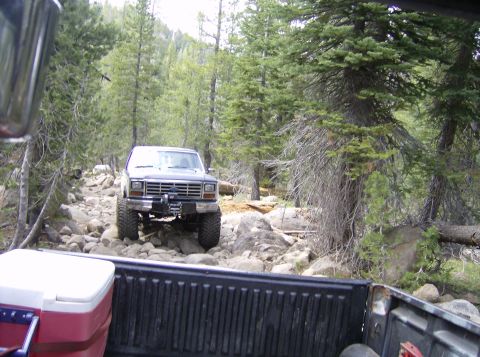 1986 Ford Bronco - A lifted Ford Bronco navigates a difficult, rocky path through a forest.