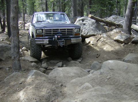 1986 Ford Bronco - A modified Ford Bronco tackles a challenging off-road course in a wooded area.