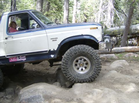 1986 Ford Bronco - Ford Bronco is shown off-roading over large rocks in a wooded area.