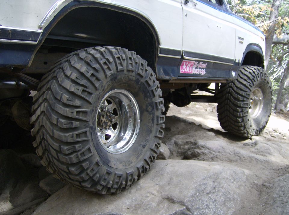 Big tires on a lifted SUV climbing over rocks. Sticker on the side says "XO-National Garage"