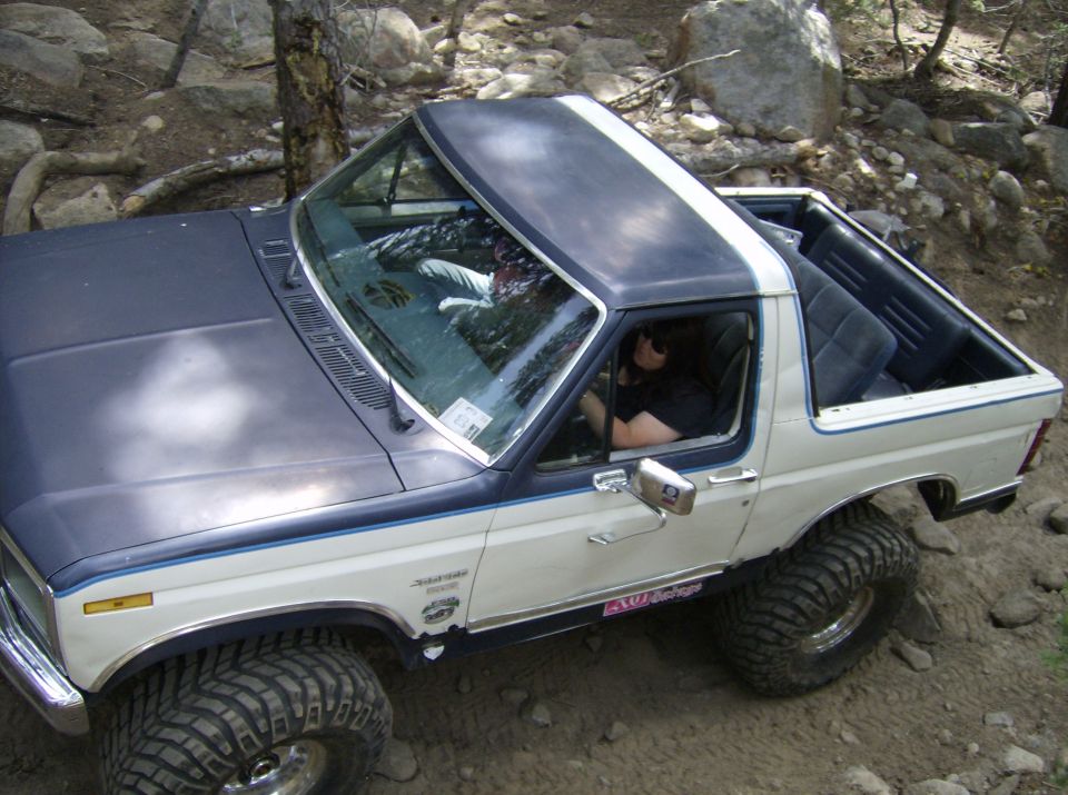 1986 Ford Bronco with lifted suspension and off-road tires navigating rocky terrain