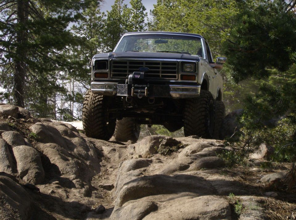 Front view of a lifted 1980s pickup truck with a winch, navigating rocky terrain