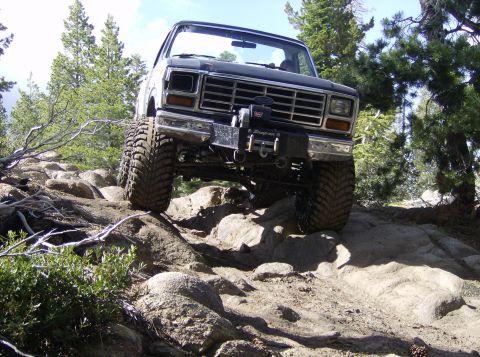 1986 Ford Bronco - This lifted truck is shown tackling a challenging rocky path in a wooded area.