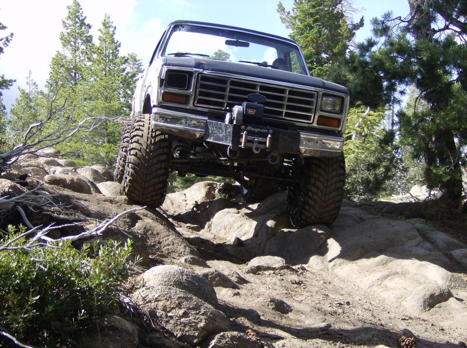 Front view of a lifted truck with large tires navigating a rocky trail. It has a winch mounted on the front bumper