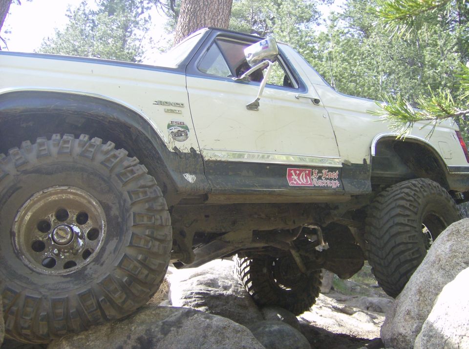 White Ford Bronco with large tires climbing over rocks on a trail