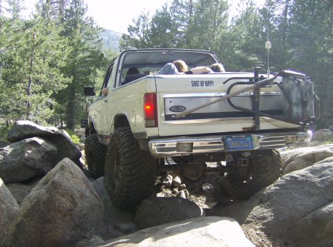 1986 Ford Bronco - White Ford Bronco tackling a rocky trail, with a 'SHUT UP HIPPY' sticker visible on the rear.