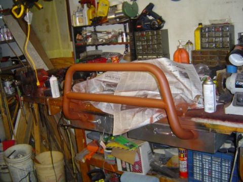 1979 Ford Bronco - A brown bull bar sits on a workbench, covered in newspaper, surrounded by tools and spray paint cans.