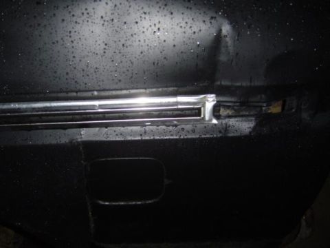 1979 Ford Bronco - Close-up of a dented black panel with chrome trim, showing water droplets on the surface.