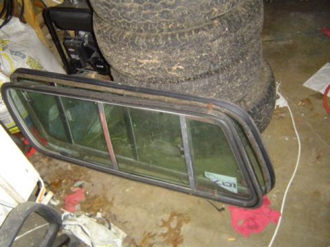 1979 Ford Bronco - A detached car window frame rests on a concrete floor next to a stack of tires.
