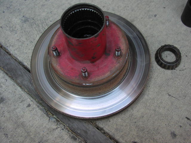 Red-painted front hub and brake rotor with wheel studs on concrete, tapered bearing beside it