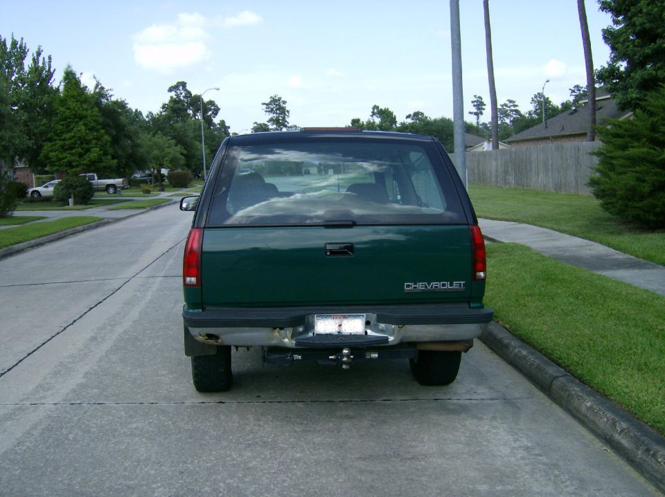 Rear view of green Chevrolet SUV parked on street. Has a trailer hitch