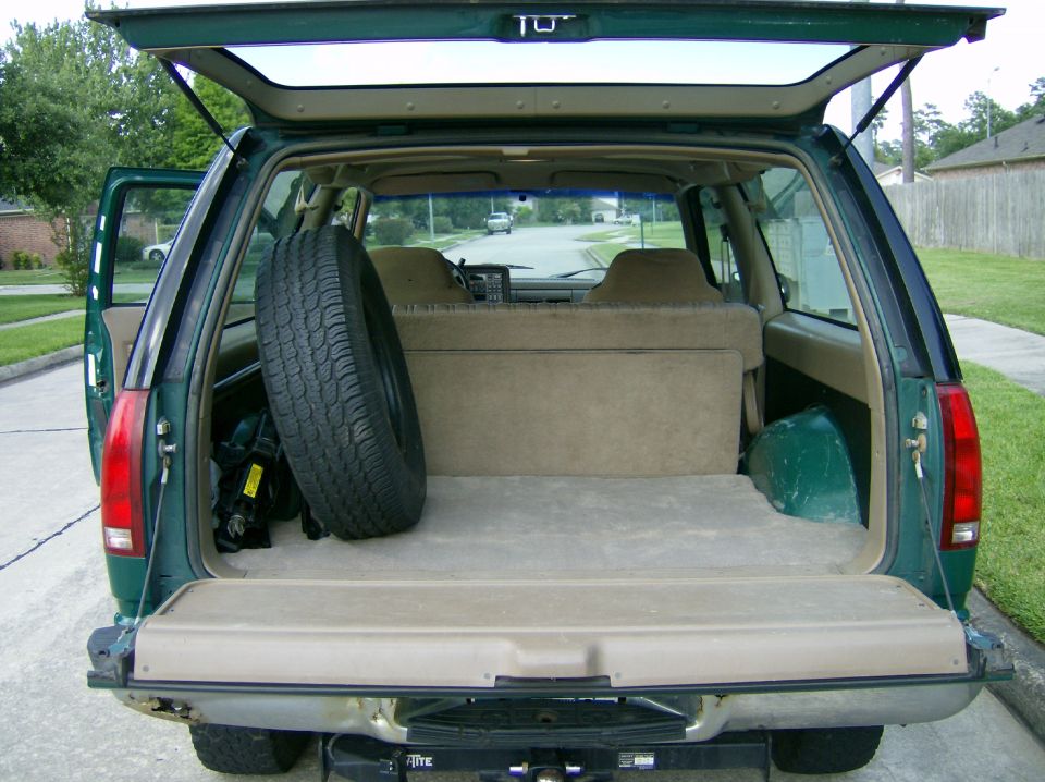 Green SUV's open cargo area with spare tire, folded seats, and a tow hitch visible