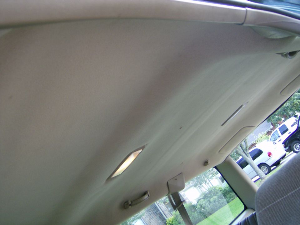 Interior ceiling of a vehicle, looking out the window at a white SUV and a dark truck