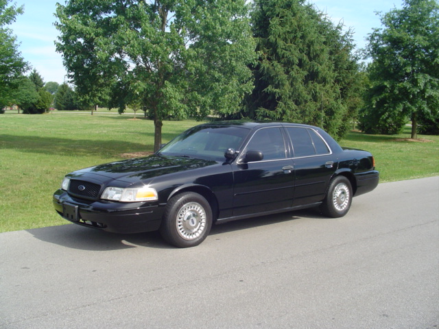 Black Ford Crown Victoria parked on a road with trees and grass in the background