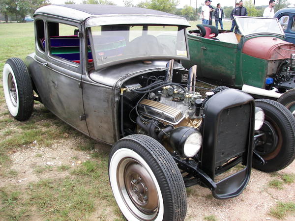 Bare metal hot rod coupe with exposed engine, whitewall tires, and custom interior